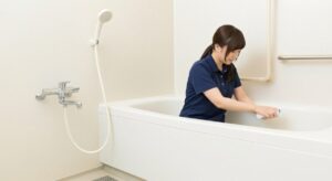 介護施設の浴室で、女性介護職員が浴槽を清掃・消毒し入浴環境の衛生管理を行っている様子