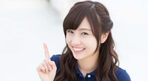 若い女性介護職員が人差し指を立てながら笑顔を見せている。介護現場でのポイント説明をイメージした場面。