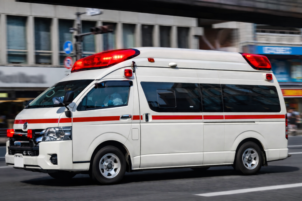 都市部の道路をサイレンを点灯させて走行する救急車。高齢者の急変や介護現場での緊急搬送をイメージした救急医療対応の様子