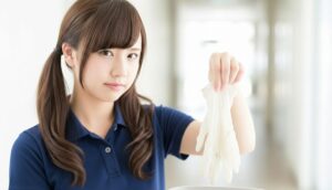 介護職員が使用済みの手袋を外して廃棄する様子。感染対策として排泄介助やケア後の適切な個人防護具(PPE)管理を行う場面